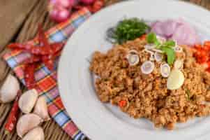 Free photo spicy minced pork salad on a white plate with red onion, lemon grass, garlic, yardlong beans, kaffir lime leaves, and spring onion