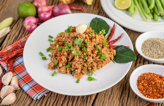 Spicy Minced Pork Salad on a white plate with red onion, lemon grass, garlic, yardlong beans, kaffir lime leaves, and spring onion