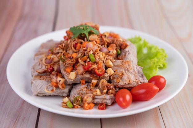 Free photo spicy pork minced with tomatoes and lettuce on a white plate on a wooden table.