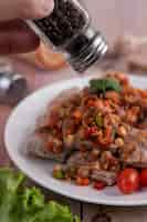 Free photo spicy pork minced with tomatoes and lettuce on a white plate on a wooden table.