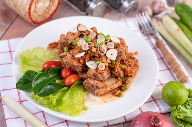 Free photo spicy pork minced with tomatoes and lettuce on a white plate on a wooden table.