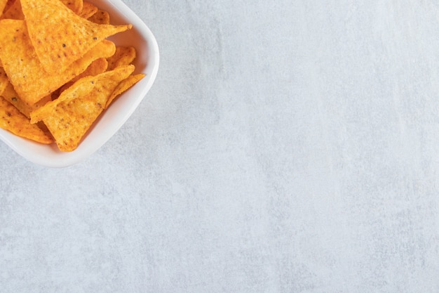 Spicy triangle chips in white bowl on stone.