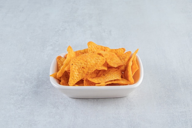 Spicy triangle chips in white bowl on stone.