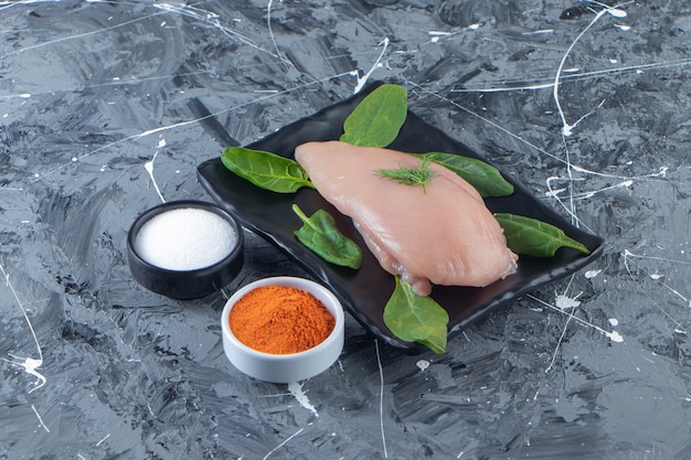 Free photo spinach and chicken breast on a platter next to spice and salt bowls , on the marble surface.