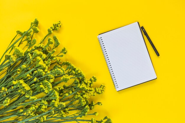 Spiral notepad and pen near the bunch of fresh flowers on yellow background