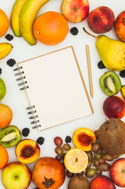 Spiral notepad and pencil surrounded with many colorful fruits