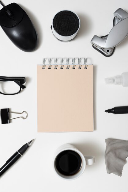 Spiral notepad surrounded by office stationery; coffee cup and eyeglass over isolated on white background