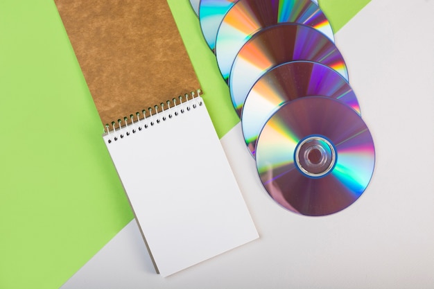 Free Photo spiral notepad with colorful compact discs on green and white dual background