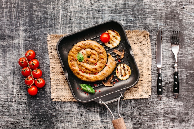 Spiral yummy grilled sausages in pan with vegetable on textured background