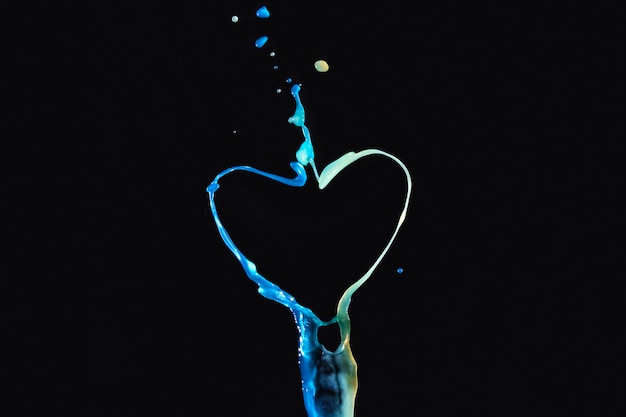 Free photo splashing colorful liquid forming heart shape over dark backdrop