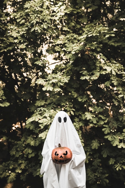 Spooky holding pumpkin near bush 