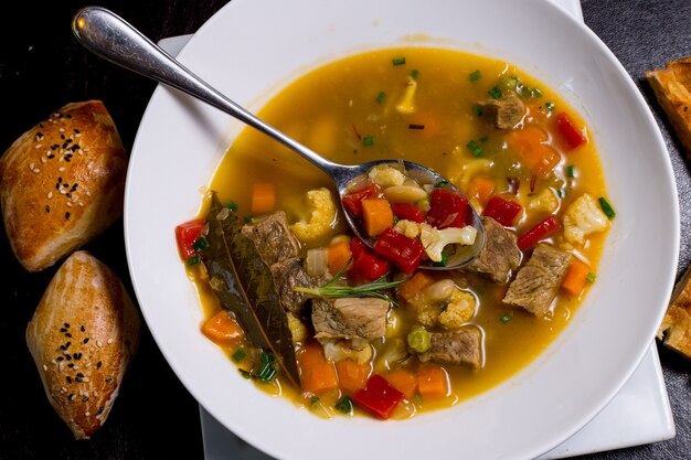 Spoon in the plate beans soup meat carrot potato tomato greens top view