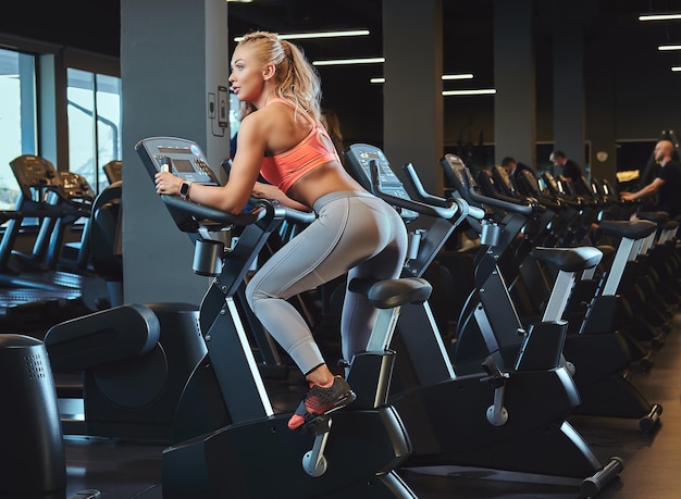 Free photo sportive blonde woman working out on an exercise bike in a modern fitness center. fitness lifestyle in sport club.