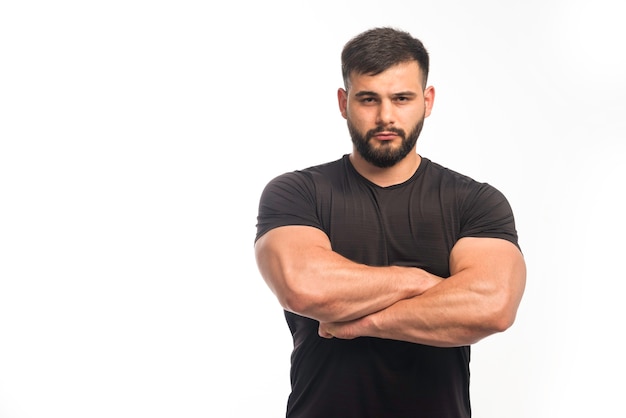 Sportive man in black shirt closing his arm muscles. 