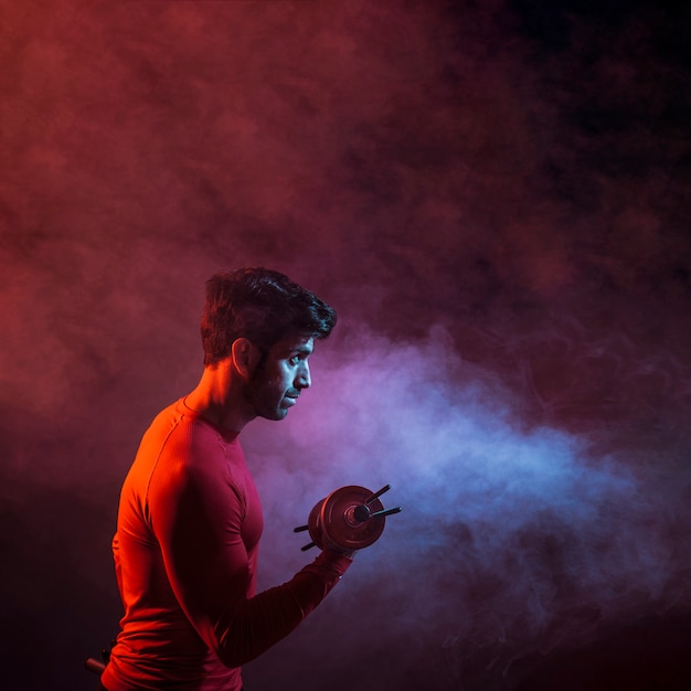 Free photo sportive man lifting dumbbell in dark