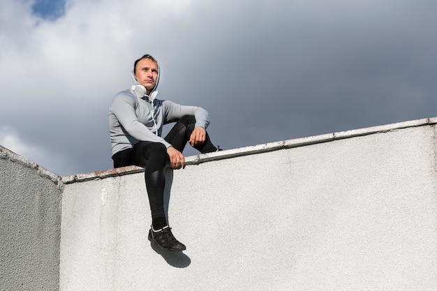 Sportive man sitting on a wall and looking away