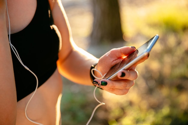 Free photo sportive woman in black tank top using a mobile phone while listening to music