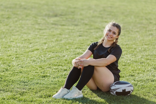 Sportive woman sitting on grass next to a ball