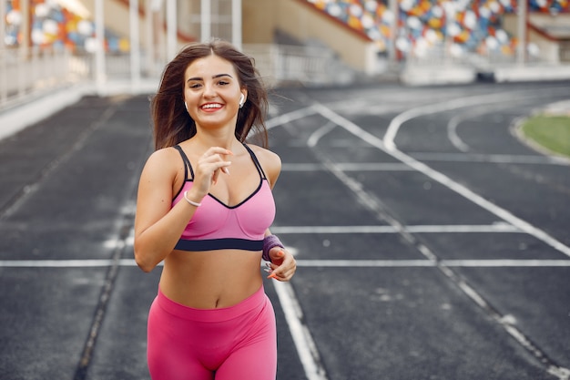 Sports girl in a pink uniform runs at the stadium