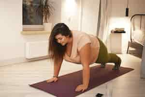 Free photo sports, healthy lifestyle, fitness and obesity concept. energetic self determined young plus size female in sportswear doing plank exercise on mat. curvy brunette woman exercising at home, planking