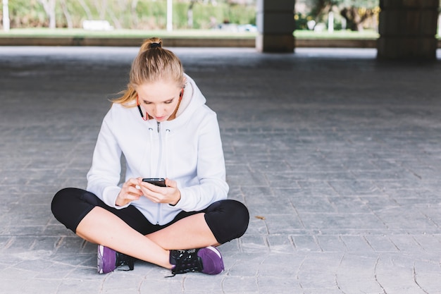 Free Photo sportswoman using smartphone on pavement