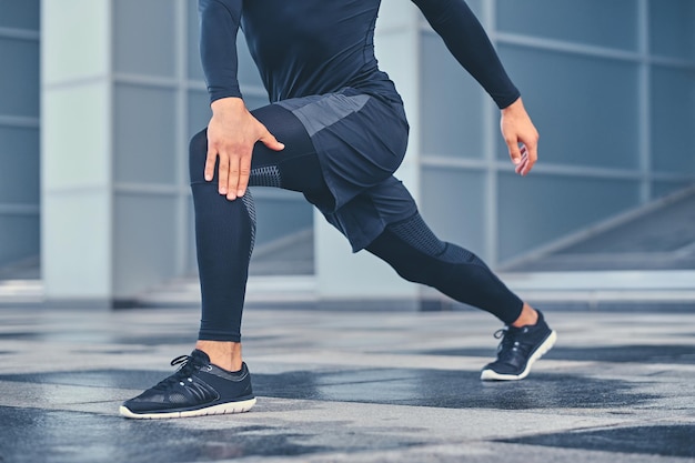 Free photo sporty athletic male is warming up and stretching outdoors over modern building background.