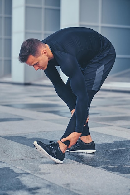 Sporty athletic male is warming up and stretching outdoors over modern building background.