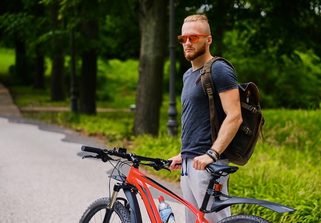 Free photo sporty bearded male sits on a red mountain bicycle outdoor.