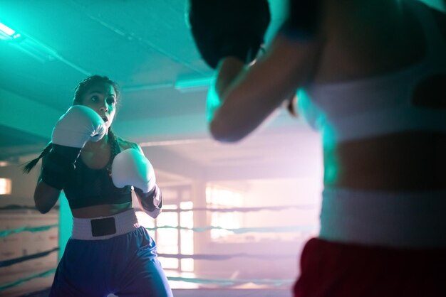 Sporty girls training fighting on boxing ring. Two Caucasian girls in sportswear and protective gloves training with each other in gym and working out punches. Womens boxing, healthy lifestyle concept