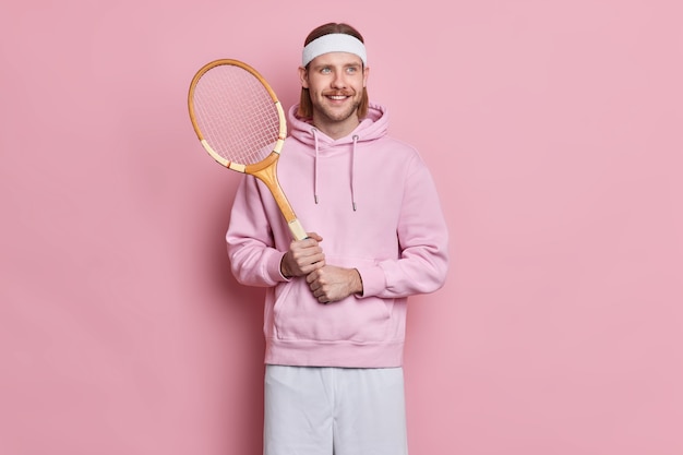 Free photo sporty satisfied active man with mustache holds tennis raquet enjoys playing favorite game during spare time