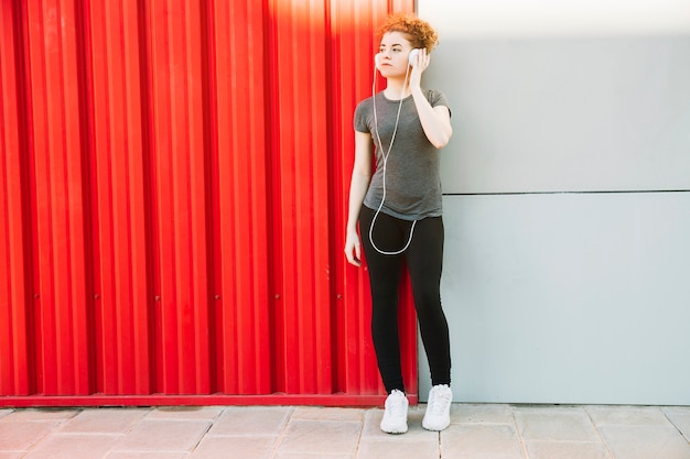 Sporty woman enjoying music near red wall