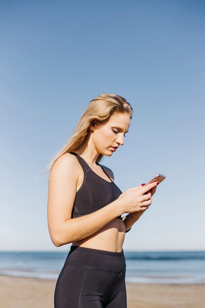 Sporty woman with smartphone at the beach