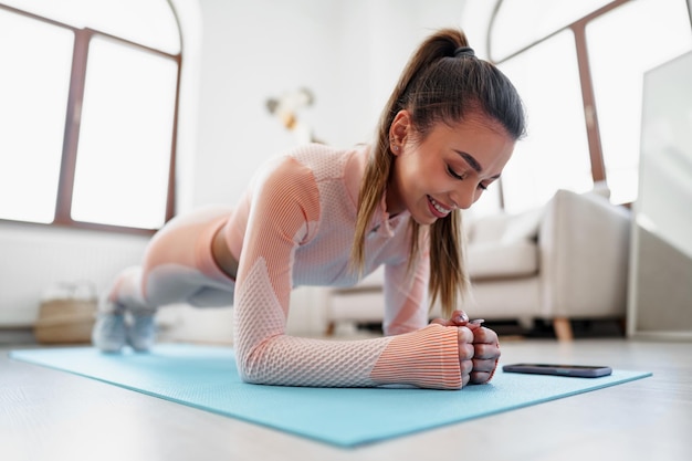 Sporty young woman doing plank exercise indoors at home