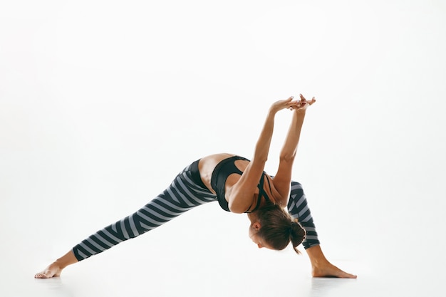 Sporty young woman doing yoga practice isolated on white  space. Fit flexible female model practicing