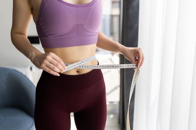 Sporty young woman and measure around her body at home.