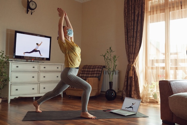 Sporty young woman taking yoga lessons online and practice at home while being quarantine. Concept of healthy lifestyle, wellness, being safe while coronavirus pandemic, looking for new hobby.