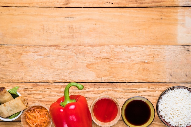 Spring roll; red bell pepper; sauces and rice bowl on wooden desk