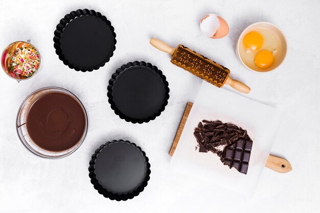 Sprinkle; egg yolk; rolling pin; chocolate bar; syrup and three empty cake holder on white background