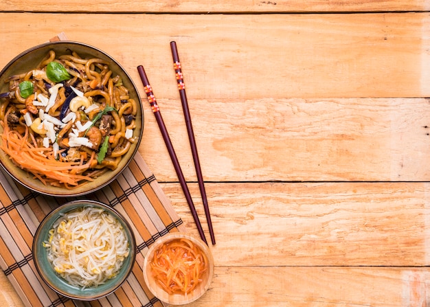 Sprouts beans; grated carrot and noodles with chopsticks over the wooden table