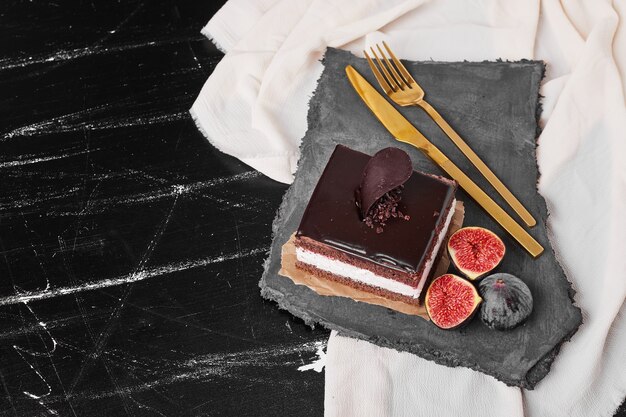 A square slice of chocolate cheesecake on a stone platter.