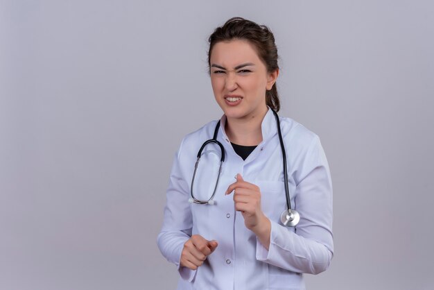 Squeamish doctor young girl wearing medical gown wearing stethoscope on white background