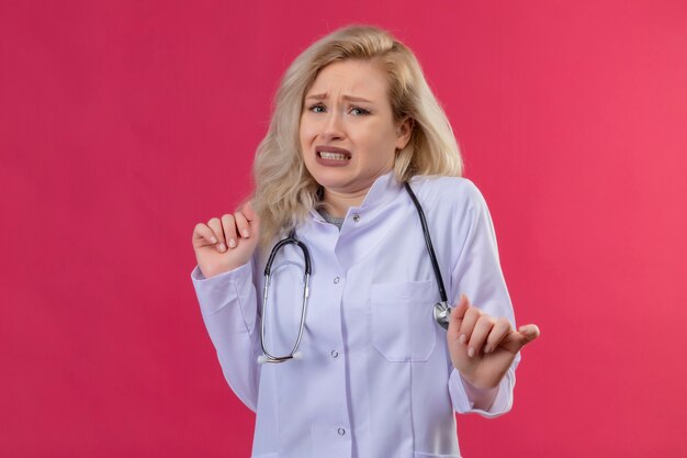 Squeamish doctor young girl wearing stethoscope in medical gown on red backgroung