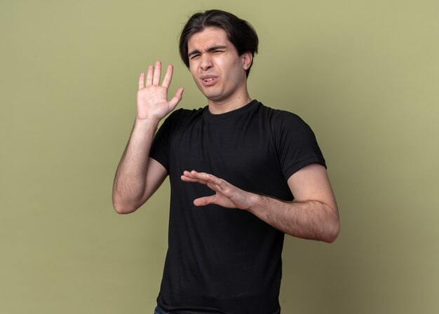 Squeamish young handsome guy wearing black t-shirt isolated on olive green wall