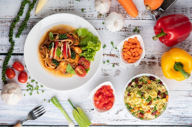 Free photo squid fried with curry paste in white plate, with vegetables and side dishes on a white wooden floor.