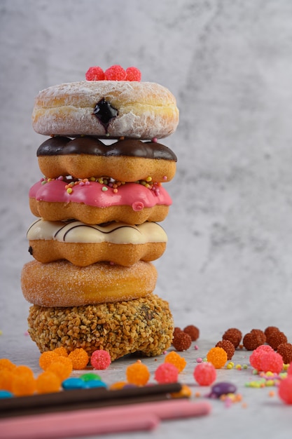 Stack of assorted donuts and topping on a white cement floor.