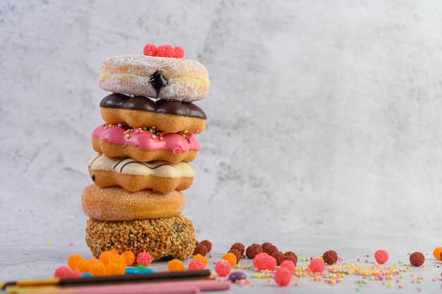 Free photo stack of assorted donuts and topping on a white cement floor.