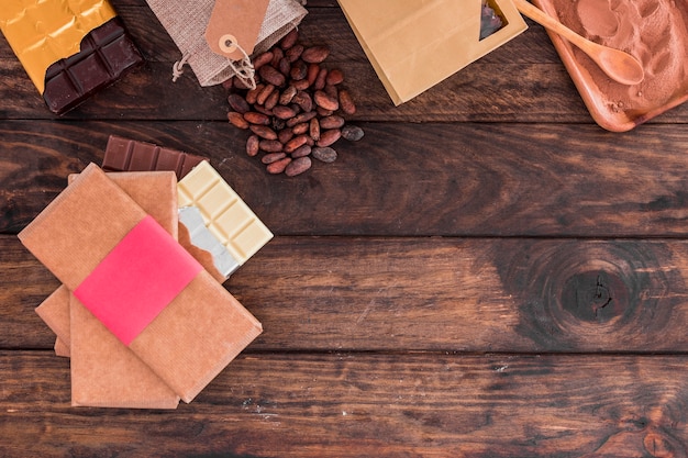 Free photo stack of chocolate bars, cocoa beans and powder on wooden desk