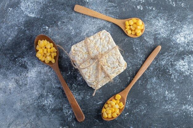 Stack of crispbread and wooden spoons of sweet corns on marble.