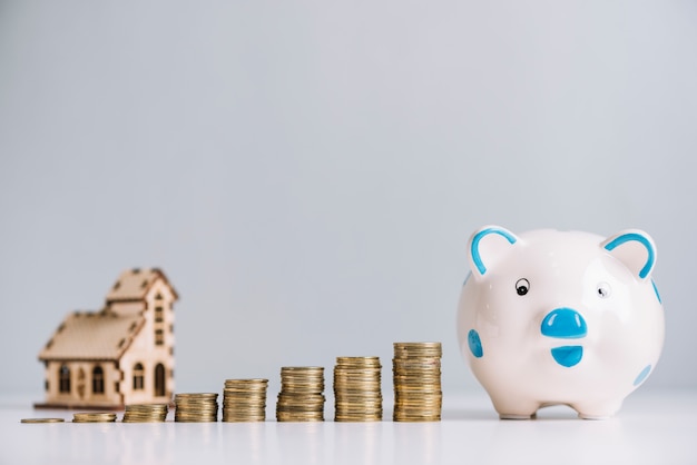 Stack of increasing coins and piggybank in front of house model