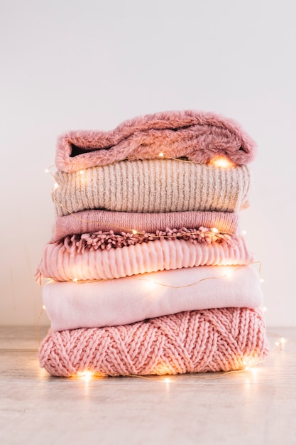 Free photo stack of knitted sweaters with garland on floor